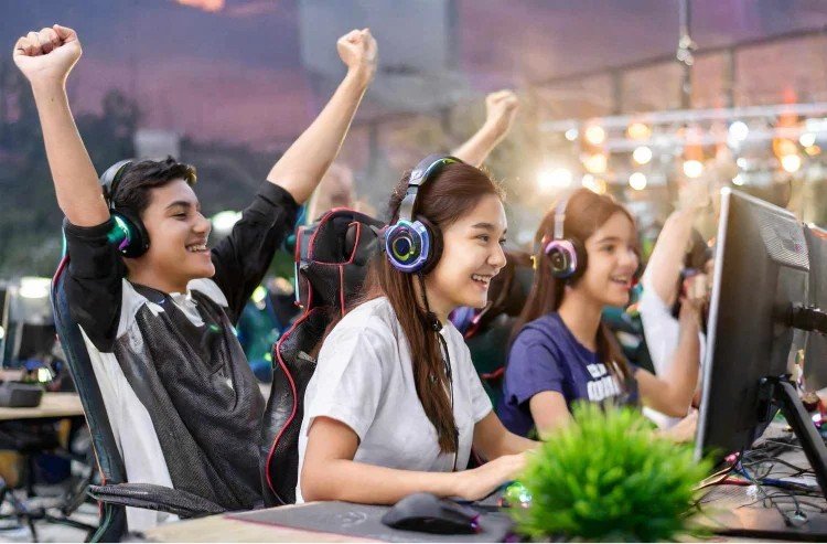 Group of young gamers celebrating victory at a gaming event, wearing headphones and sitting at computer stations.